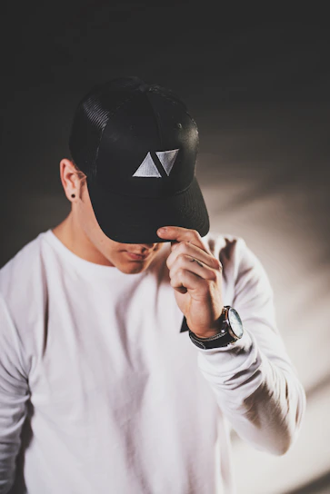A close-up of a hand adjusting a sleek black baseball cap with the capella logo embroidered on the front.
