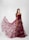 A woman stands elegantly in a studio setting, showcasing a long and flowing maroon gown adorned with small floral embellishments. The dress features a strapless design with intricate detailing on the bodice and a sheer overlay that creates a dramatic train.