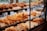 A pastry display case filled with various types of bread and baked goods, including baguettes, rolls, pretzels, and pastries with different shapes and textures. The baked items are arranged in rows on wooden shelves behind a glass front, with a variety of golden brown hues indicating a freshly baked assortment.