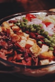 A colorful salad featuring a variety of fresh ingredients, including croutons, red cabbage, kidney beans, green peas, cherry tomatoes, and sliced onions, all displayed in a large bowl.