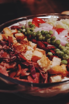 A colorful salad featuring a variety of fresh ingredients, including croutons, red cabbage, kidney beans, green peas, cherry tomatoes, and sliced onions, all displayed in a large bowl.