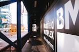An urban construction area with a sign displaying 'Brookfield Multiplex' on a black background. A truck is visible on the street with orange safety barriers nearby. Skyscrapers and other buildings can be seen in the background.