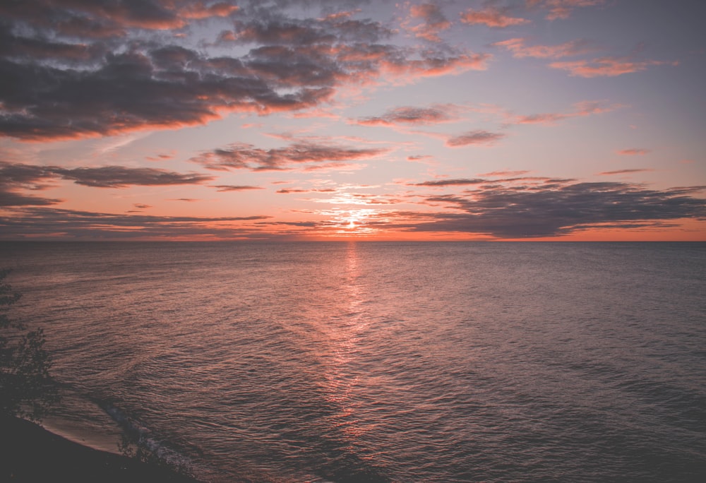 body of water under gray sky at golden hour