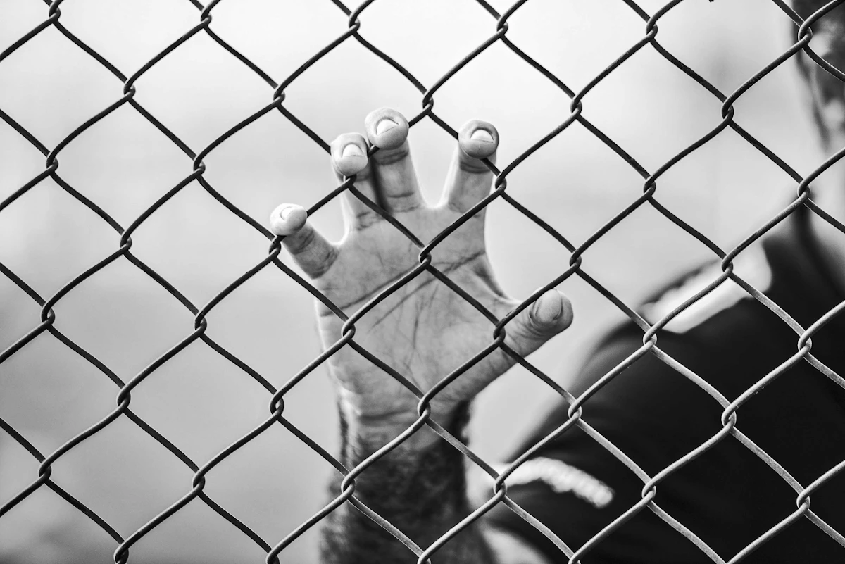 A hand gripping a chain-link fence in contemplation