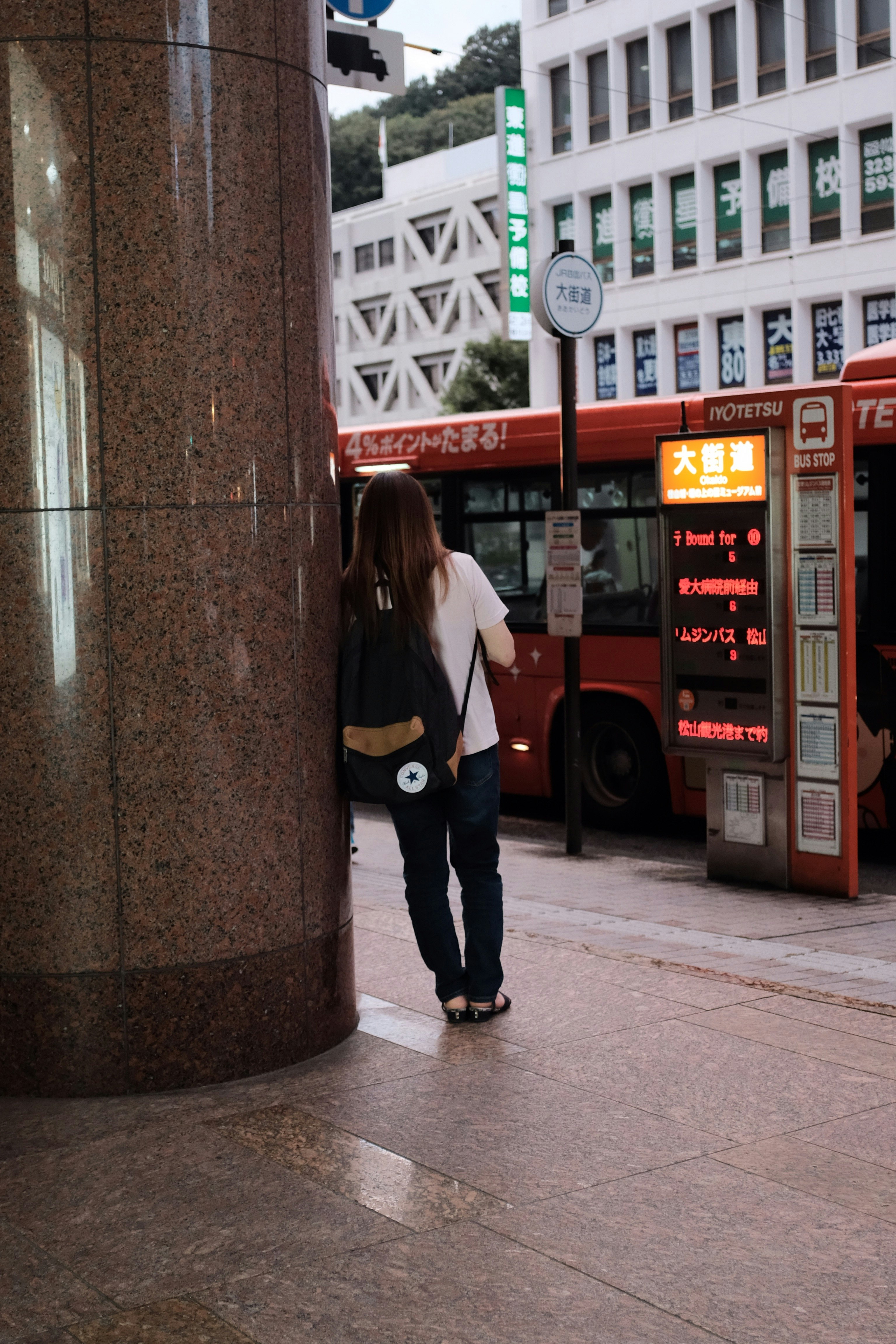 person carries black Converse backpack while leaning on the pillar