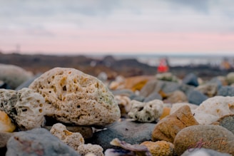 Close-up of natural stone keychains with lighthouse logo on rocky seaside background.