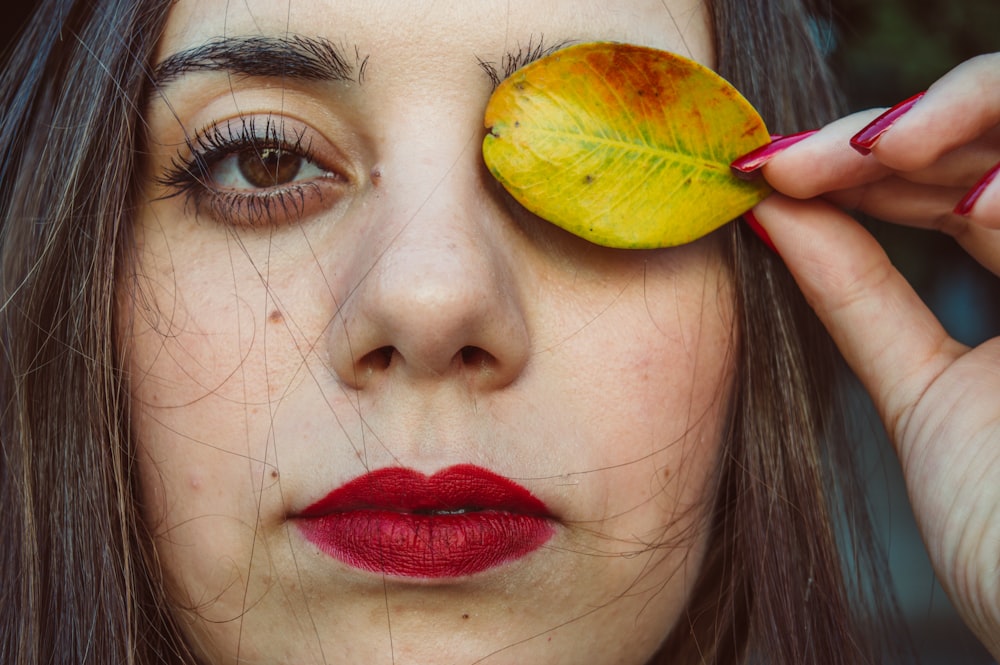 woman covering her left eye with yellow leaf