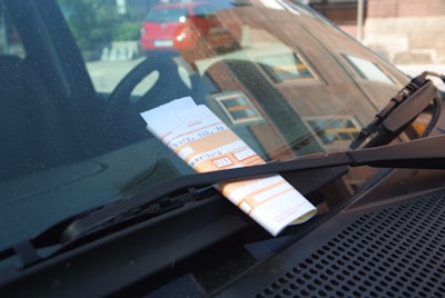 Close-up of a traffic ticket on a car windshield with a blurred city street in the background
