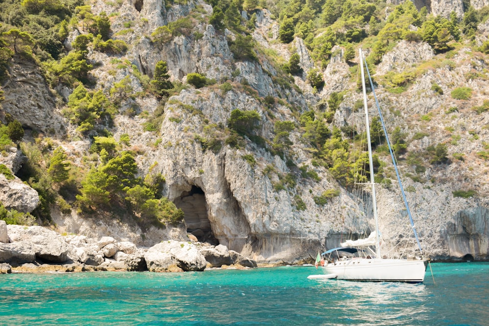 a sailboat in the water near a rocky cliff