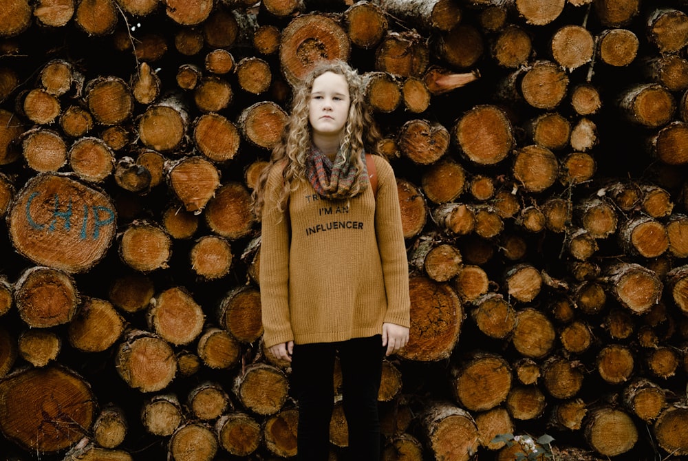 a young girl standing in front of a pile of logs