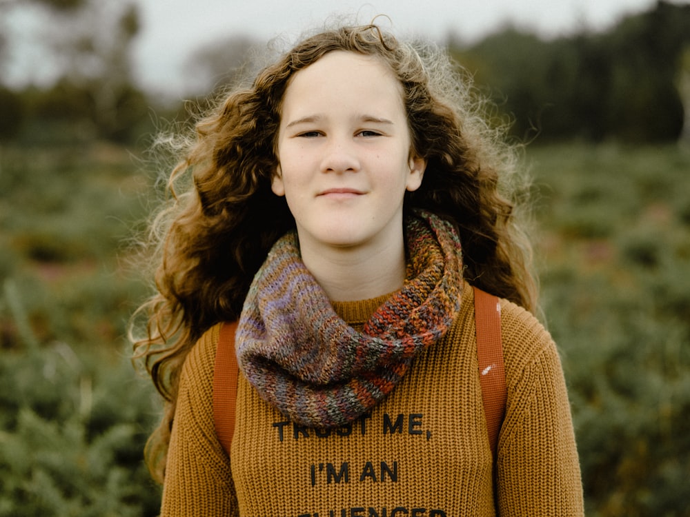 a girl with curly hair wearing a sweater and a scarf