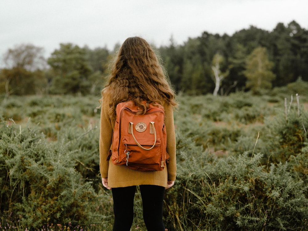 woman carrying backpack standing on grass during day