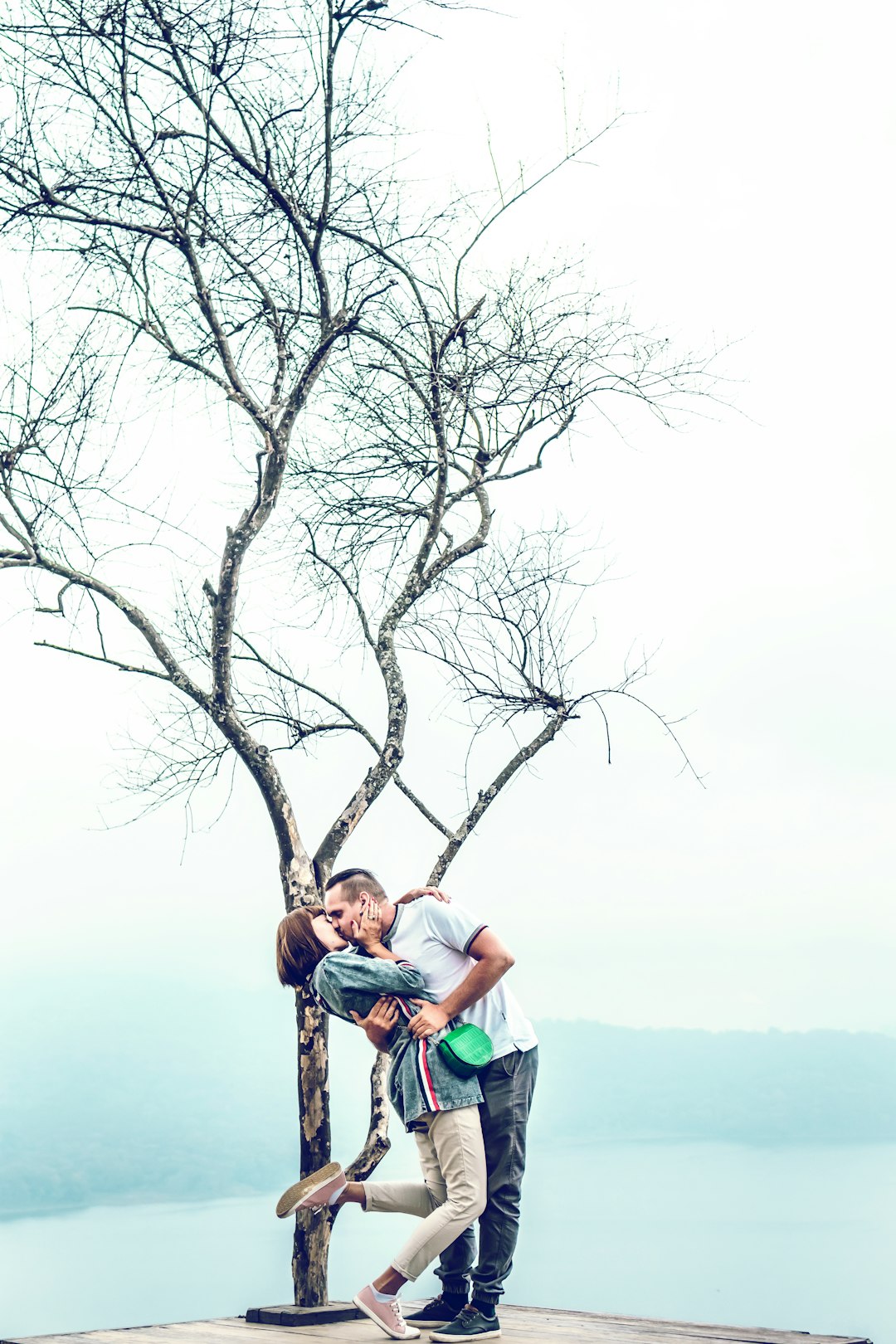 man and woman kissing beside tree
