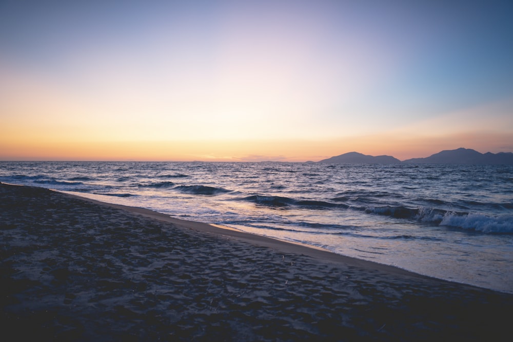 the sun is setting over the water at the beach