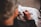 An elderly person is sewing or embroidering on a piece of white fabric, with detailed focus on their hands. The lighting is warm and soft, highlighting the texture of the skin and fabric.