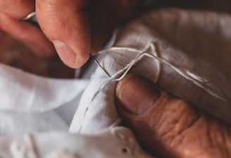 Close-up of hands sewing delicate fabric in a sunlit workshop.