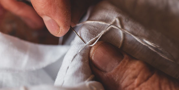 Close-up of hands sewing delicate fabric in a sunlit workshop.