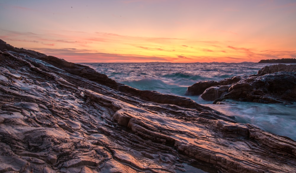 the sun is setting over the ocean and rocks