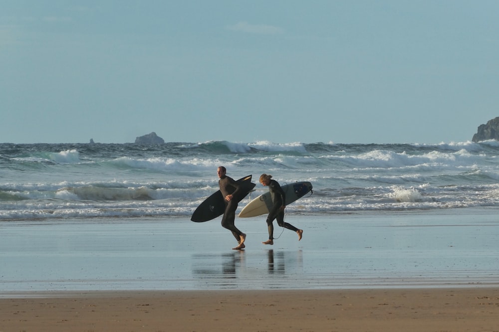 man and woman holding surfboards running near seashore under blue and white skies during daytime