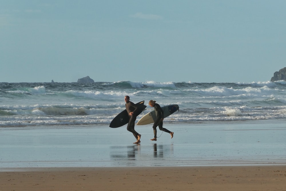 Hombre y mujer sosteniendo tablas de surf corriendo cerca de la orilla del mar bajo cielos azules y blancos durante el día