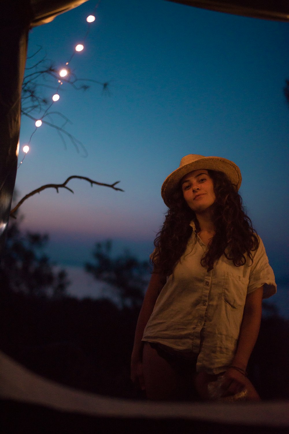 a woman wearing a hat standing next to a tree