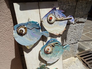 Close-up of a colorful ceramic fantasy fish hanging on a rustic outdoor wall.
