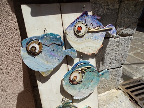 Close-up of a colorful ceramic fantasy fish hanging on a rustic outdoor wall.