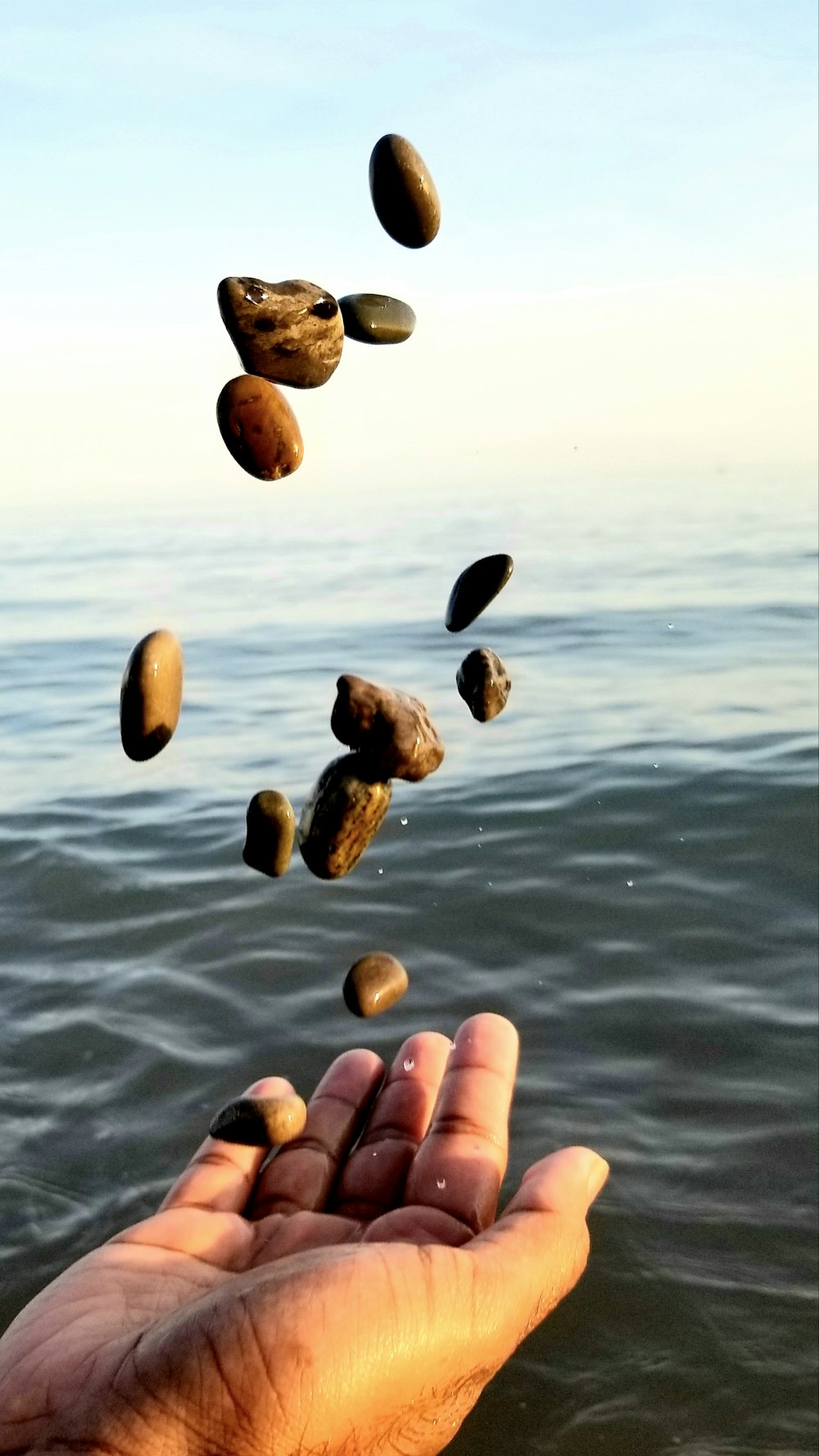 person throwing stones on blue sea