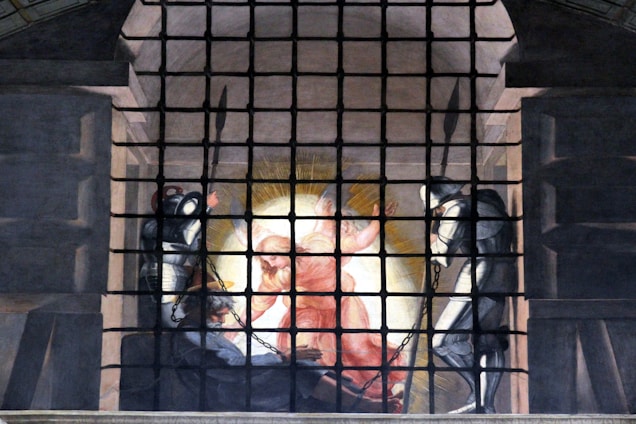 A scene depicting an angelic figure in a celestial glow, surrounded by dark armored guards. The angel appears radiant and ethereal in the center, drawing attention with vibrant light, while the guards stand solemnly on either side, clad in metal armor and chains, in a dimly lit, prison-like setting.