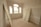 An empty room with unfinished drywall and three uninstalled white doors leaning against the walls. The room features three large windows with wooden frames and an arched central window, allowing natural light to flood in and revealing a view of the outside.