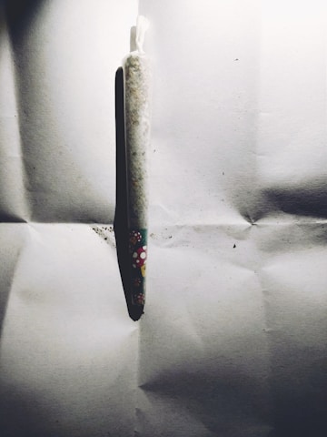A tightly rolled cigarette or joint wrapped in paper featuring colorful mushroom designs resting on a crumpled white surface. Shadows are cast, enhancing the contrast with the background.