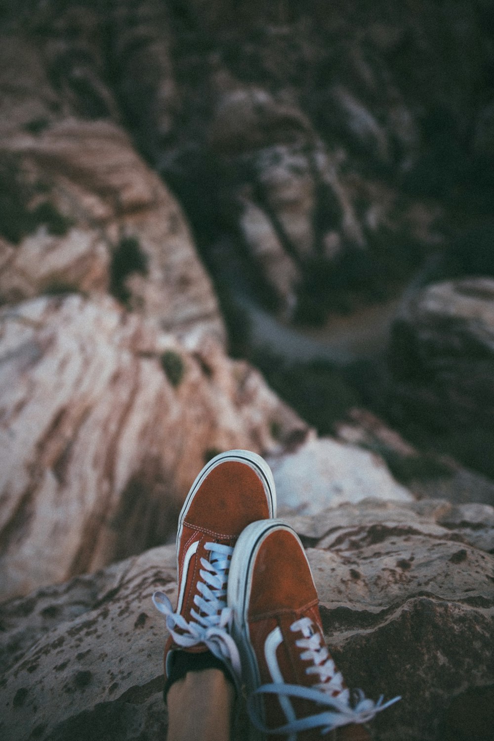 person sitting on cliff wearing brown-and-white Vans low-top sneakers