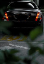 A sleek black saloon car parked outside a London airport terminal at dusk.