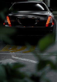 A sleek black saloon car parked outside a London airport terminal at dusk.