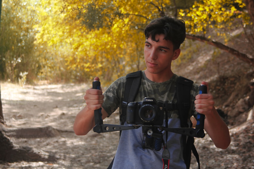 man holding camera stabilizer beside trees