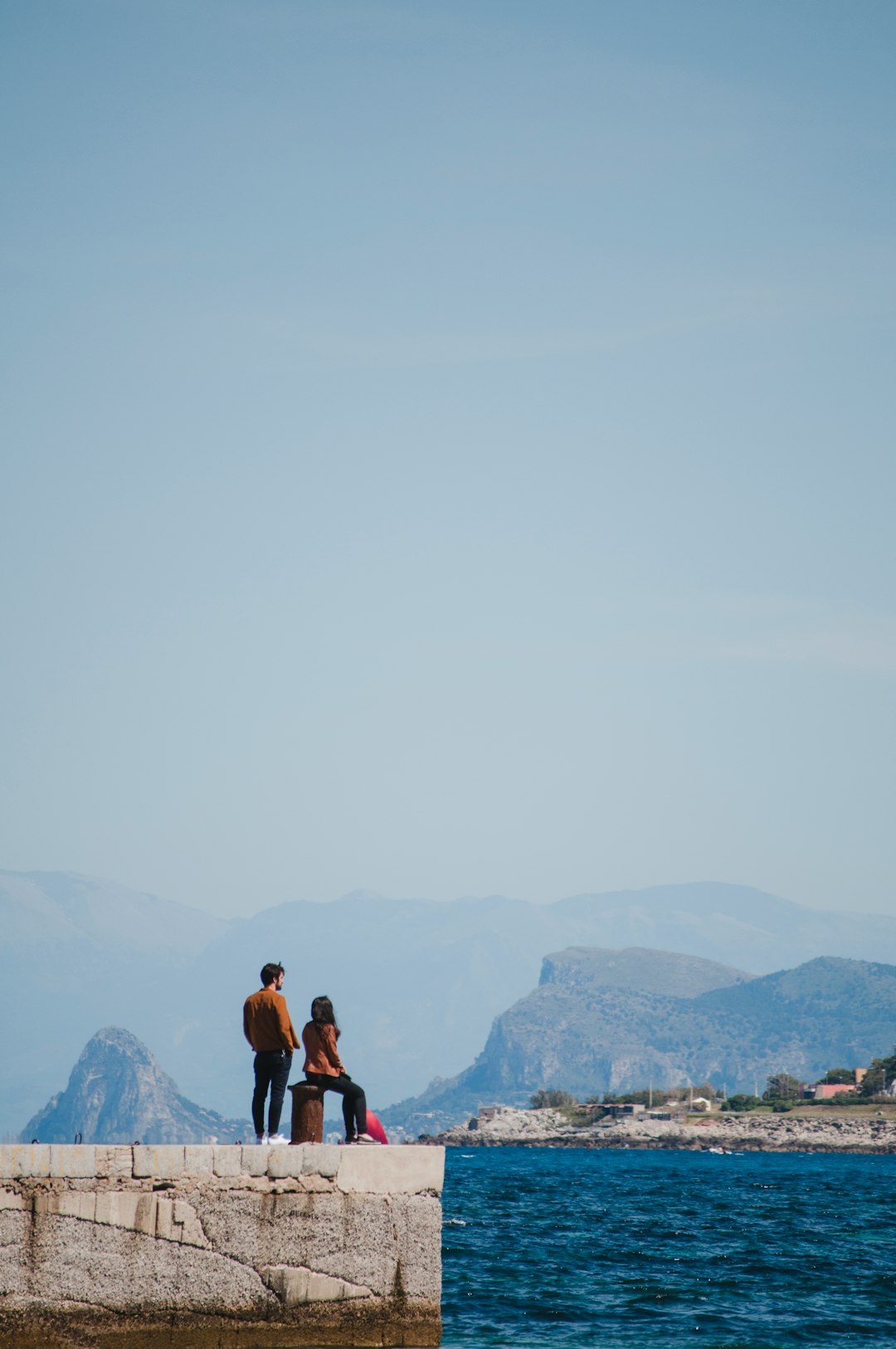man and woman on concrete platform facing ocean