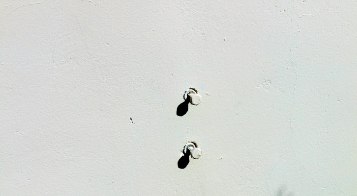 A plain surface with two small protruding screws casting shadows below them. The wall is light-colored and textured.