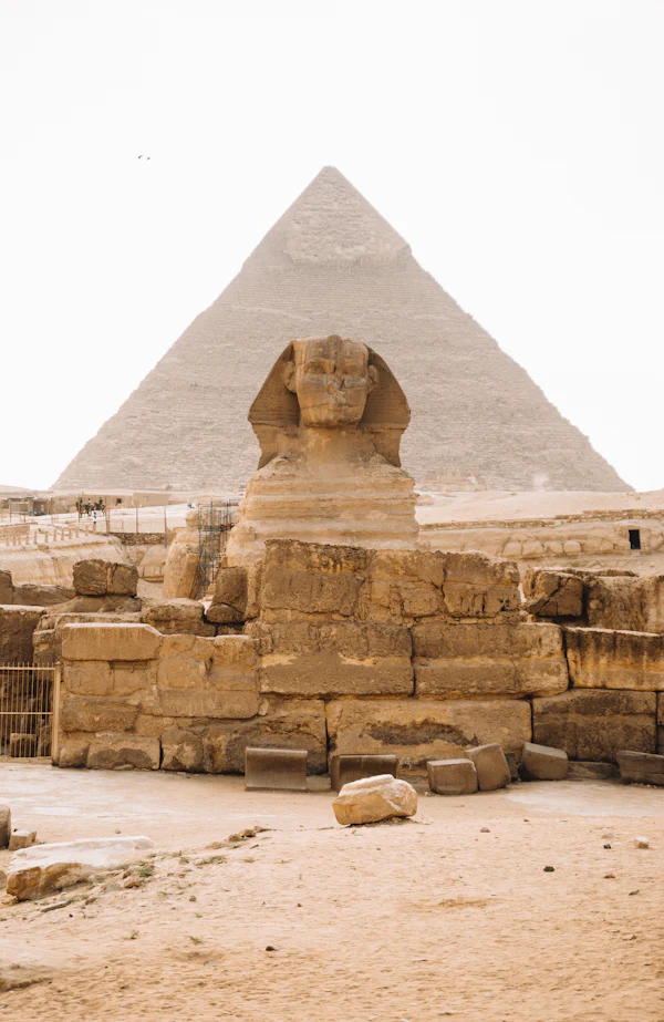 The Great Sphinx in front of a pyramid under a pale desert sky