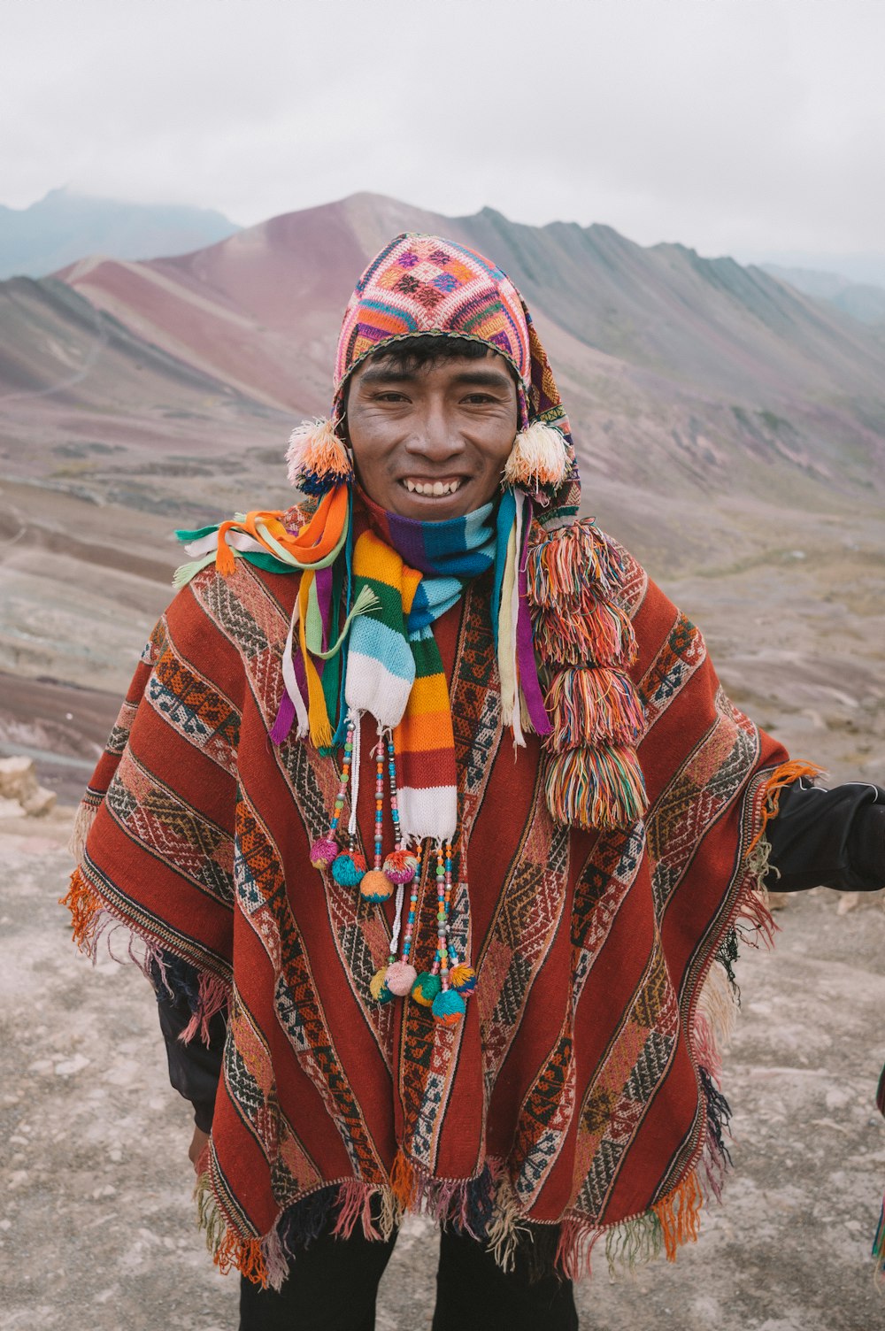 homem sorridente em pé na frente das montanhas durante o dia