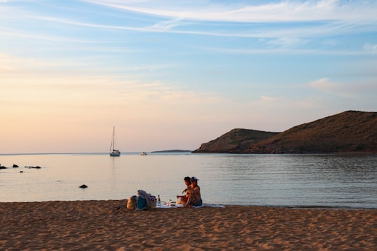 two persons sitting on seashore during day in Menorca Spain