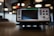 A Keithley data acquisition and multimeter system placed on a table. The device features a large screen with surrounding control buttons and various input ports. The background is softly blurred, suggesting an office or laboratory environment, with circular lights visible.