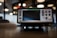 A Keithley data acquisition and multimeter system placed on a table. The device features a large screen with surrounding control buttons and various input ports. The background is softly blurred, suggesting an office or laboratory environment, with circular lights visible.