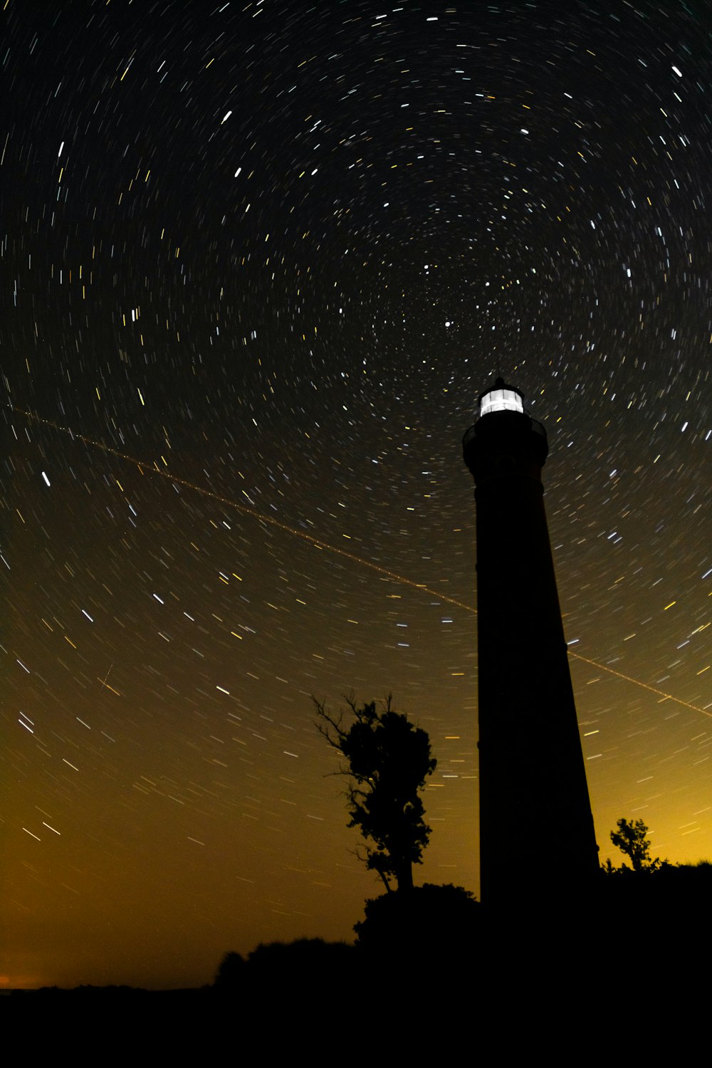 a lighthouse with a star trail in the sky