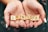 Hands are gently cupping a set of wooden Scrabble tiles spelling out the word 'SENIOR'. The tiles have a light wood grain finish, and the hands have neatly manicured nails with white polish, set against a blurred green background.