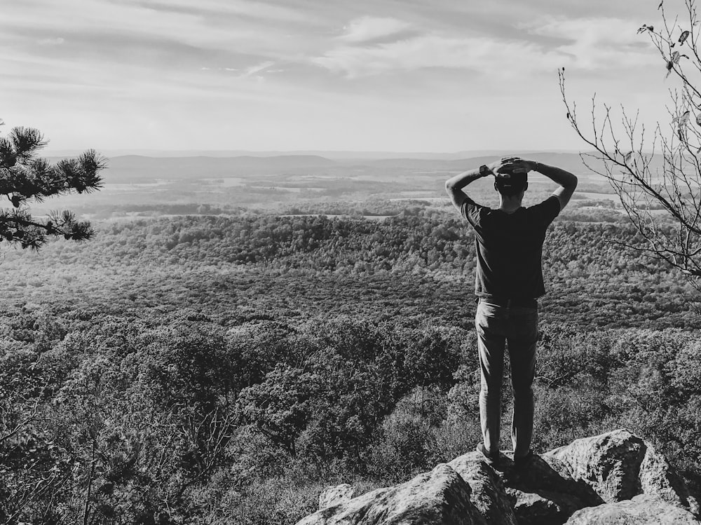 grayscale photography of man standing on rock