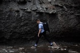 A man wearing a waterproof jacket crossing a shallow stream with mossy rocks.