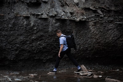 A man wearing a waterproof jacket crossing a shallow stream with mossy rocks.