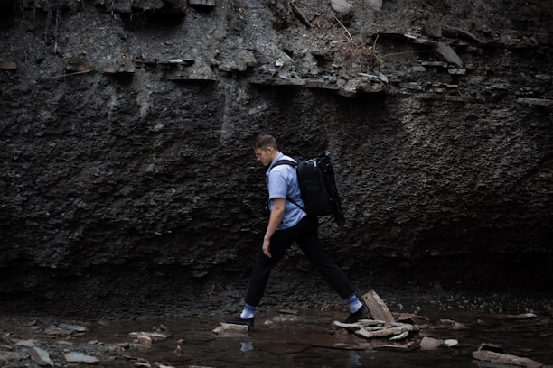 A hiker crossing a rocky stream with minimalist survival gear, showcasing mobility and light packing.