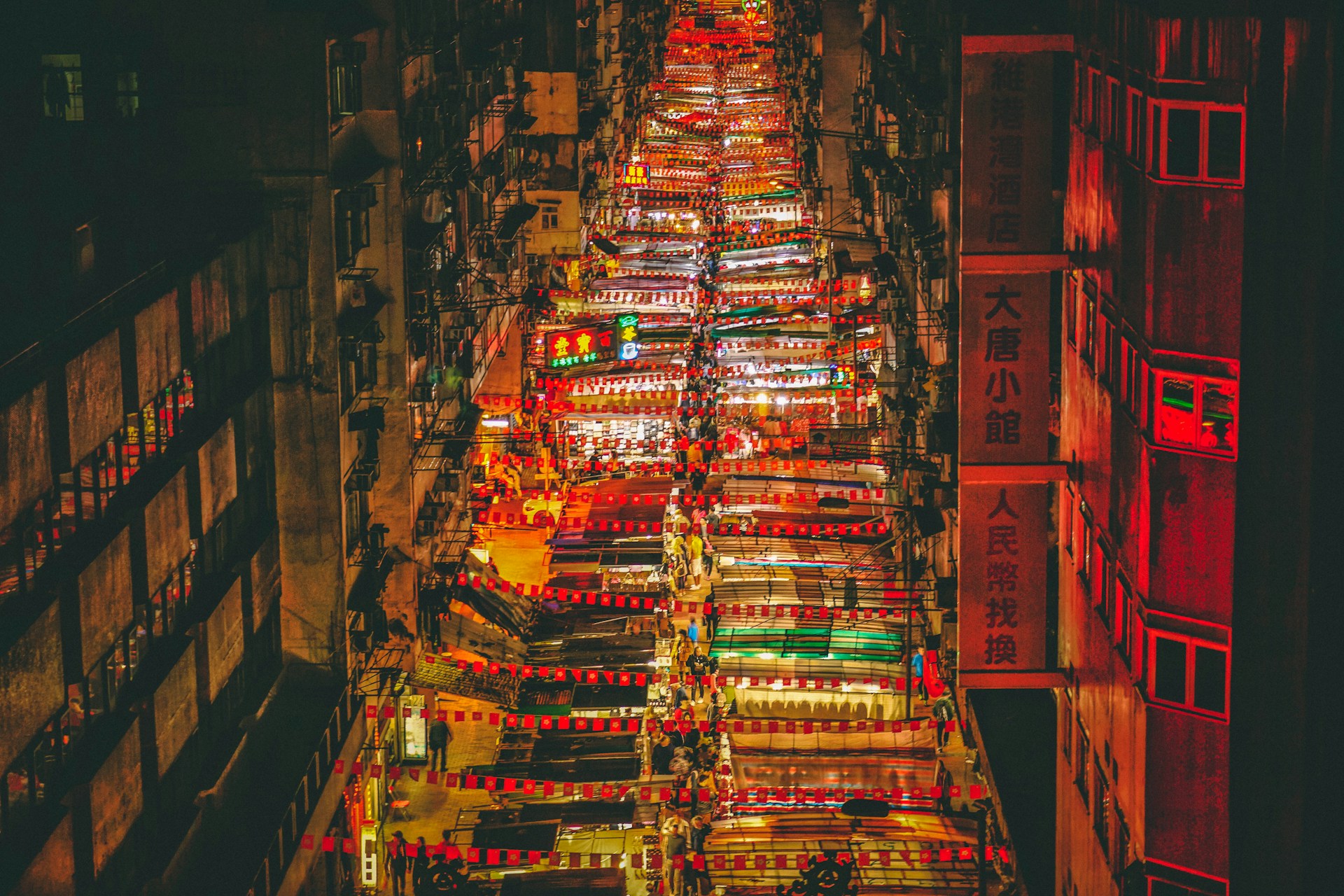 A vibrant street market in Bangkok bustling with colorful stalls and lively crowds under warm evening lights.