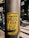 A yellow sticker on a weathered metal pole featuring bold black text that appears political in nature. The background shows an urban environment with blurred buildings and a street.